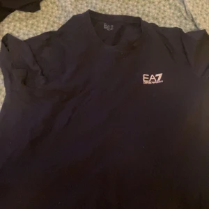 Svart t-shirt från Emporio Armani - Säljer en svart t-shirt från Emporio Armani, EA7. Den är i mycket bra skick och har en enkel design med EA7-loggan på bröstet. Perfekt för vardagsbruk eller träning. Storlek L och tillverkad i ett mjukt material.
