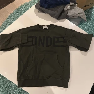 Olivgrön sweatshirt från Dondup - Säljer en olivgrön sweatshirt från Dondup, Made in Italy. Den har en stor ficka framtill och texten 'DNDP' tryckt över bröstet. Perfekt för en avslappnad stil och passar bra till både jeans och joggers. Skön och stilren design!