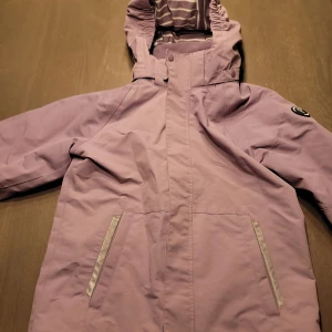 Lila jacka från Polarn O. Pyret - Säljer en superfin lila jacka från Polarn O. Pyret i storlek 140, passar 9-10 år. Perfekt för höst och vår med sin långa ärmar och praktiska huva. Jackan har en snygg design med dragkedja och knappar framtill. Den är i mycket bra skick och redo för nya äventyr!