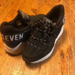 Svarta sneakers från Sixtyseven - Säljer ett par svarta sneakers från Sixtyseven i bra skick. Skorna har en cool design med vit sula och textdetaljer på hälen. De är gjorda i mocka och textil och har snörning framtill. Perfekta för vardagsbruk eller en avslappnad dag ute. Tyvärr saknas ett snöre och innersulor, men det är lätt att komplettera