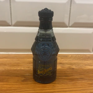 Versace Blue Jeans parfym - Säljer en cool Versace Blue Jeans parfym i en unik blå flaska som ser ut som en jeansbyxa. Flaskan har en snygg design med Versace-loggan och en gul text. Perfekt för dig som vill ha en fräsch och ungdomlig doft. Passar både till vardags och fest! 75ml