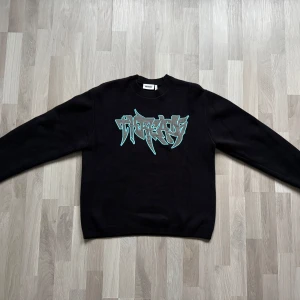 Stickad Weekday Tröja med Tryck (Graffiti)  - En mysig svart jacquardtröja gjord av  mjuk 100% ekologisk bomull. Den är löst sittande och har ordet ’threads’ broderade i graffiti över bröstet.  Använts endast 1 gång!  Skicka gärna ett meddelande ifall du vill se fler bilder.
