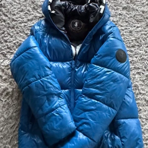 Blå pufferjacka från Save the Duck - Säljer en snygg blå pufferjacka från Save the Duck i storlek M. Jackan är 100% animal free och har en dragkedja framtill. Den är perfekt för vintern och den håller kylan grymt bra! Den har en cool logga på ärmen och är supervarm och bekväm. Perfekt för kalla dagar! Skicket är 8/10 och har använts under en vinter