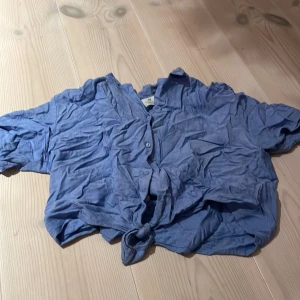 Blå knytblus från H&M - Säljer en blå blus från H&M i storlek EUR 158. Den har korta ärmar och en snygg knytning framtill. Perfekt för sommardagar eller en avslappnad vårlook. Materialet känns lätt och luftigt, vilket gör den bekväm att bära. Passar både till jeans och kjol!