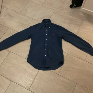 Blå skjorta från Ralph Lauren - Säljer en snygg blå skjorta från Ralph Lauren i storlek M men passar S. Skjortan har en slim fit passform och är långärmad med knappar framtill. Perfekt för både vardag och fest! 💙
