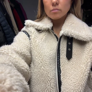 Beige teddyjacka med dragkedja - Säljer en supermysig beige teddyjacka med dragkedja och svarta detaljer som är köpt förra vintern. Perfekt för kalla dagar när du vill vara både varm och snygg. Jackan har en krage som går att vika upp och även lite längre ärmar, superskön till höst och vinter. Den är i mycket bra skick och säljer för att jag köpt en ny vinterjacka!🩷