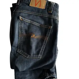 Säljer ett par snygga mörkblå jeans från Nudie Jeans i storlek 32/34 i low slim Jim modellen. De har en klassisk femficksdesign med orange sömmar och en bekväm passform. Hör av er om frågor!!