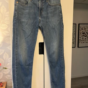 Blå jeans 502 från Levi's  - Säljer ett par klassiska blå Levi's jeans i mycket bra skick. Modell 502. De har en straight passform och är perfekta för vardagsbruk. Jeansen har en traditionell femficksdesign och är tillverkade i slitstarkt denim.