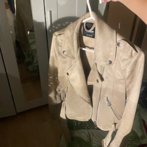 Beige skinnjacka från pull and bear  - Snygg beige skinnjacka från pull and bear i mycket bra skick. Den har en cool bikerstil med dragkedja och knappar. Perfekt för höst och vår, och funkar lika bra till fest som till vardags. Jackan är croppad och har långa ärmar. En riktig garderobsfavorit!