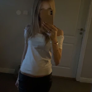 Vit offshoulder topp - Säljer en stilren vit offshoulder topp. Den har en tight passform och ärmlös design som ger en snygg och modern look. Toppen är i mycket bra skick och passar perfekt till både jeans och kjol.