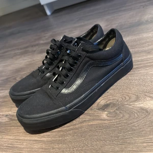 Svarta sneakers från Vans - Säljer ett par klassiska svarta Vans sneakers i mycket bra skick. De har en stilren design med snörning och en diskret vågig detalj på sidan. Perfekta för vardagsbruk och passar till nästan allt. Storlek är inte angiven, men de ser ut att vara i standard herrstorlek.