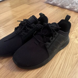 Svarta sneakers från Adidas - Säljer ett par svarta Adidas sneakers i mycket bra skick. De har en stilren design med snörning och en bekväm sula. Perfekta för både vardag och träning. Skorna är i syntetmaterial och har en diskret Adidas-logga på sulan.