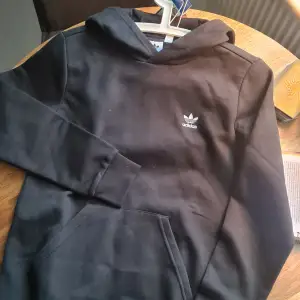 En svart hoodie från Adidas originals, helt oanvänd (nypris 500:-). Säljer pga felköp. Det är den klassiska designen. Storlek M/158. Skriv för fler frågor!