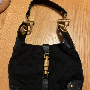 Gucci väska  - Säljer en äkta elegant svart axelväska från Gucci i mycket bra skick. Väskan har snygga gulddetaljer och ett diskret mönster. Perfekt för både vardag och fest! 🖤