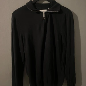 Svart tröja med dragkedja - Säljer en stilren svart tröja med dragkedja vid halsen. Perfekt för både vardag och lite kyligare dagar. Tröjan har långa ärmar och en ribbad krage som ger en snygg look. Passar bra till jeans eller chinos!