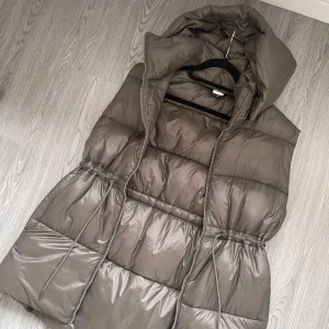 McKinley väst storlek S - Super snygg shiny vadderad väst, med stora fickor och snörning i midjan. Går över rumpan Avtagbar luva Använd enstaka gånger, i nyskick.  Färgen är militärgrön/khaki.