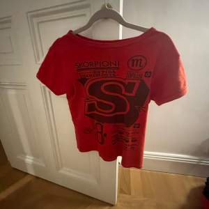 Säljer en cool röd t-shirt med svart tryck och text. Perfekt för en avslappnad stil. T-shirten är kortärmad och har en normal passform. Det står ingen storlek men skulle tippa p xs/s.