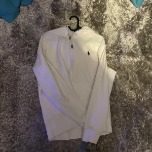 Vit hoodie Ralph Lauren - Säljer en stilren vit hoodie från Ralph Lauren i mycket bra skick. Den har en dragkedja framtill och den klassiska loggan broderad på bröstet. Perfekt för både vardag och chill. Passar till alla säsonger och är superbekväm!
