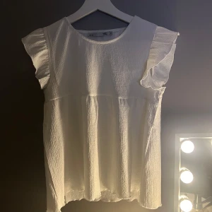 Vit blus med volangärmar - Säljer en söt vit blus från lager 157 i storleken 160cm. Den har volangärmar och ett luftigt, texturerat material. Perfekt för sommardagar eller en avslappnad vårlook. Passar både till jeans och kjol! Denna är ifrån barnavdelningen på lager 157 och endast provad och aldrig använts! Denna är perfekt i läng på mig som är 162-163 men sitter tyvärr för tight vid bysten❤️