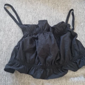 Svart topp från H&M Divided - Säljer en svart topp från H&M Divided i storlek 40. Toppen har smala axelband och en elastisk design som ger en bekväm passform. Perfekt för sommarens varma dagar eller som ett lager under en jacka. Har aldrig använt.