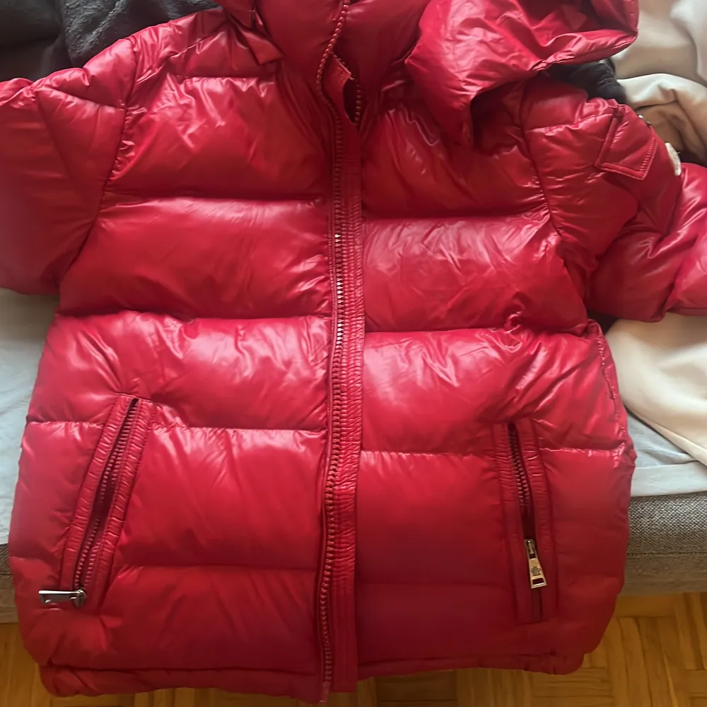 Säljer en snygg röd dunjacka från Moncler i mycket bra skick. Jackan har en quiltad design med dragkedja och en praktisk huva. Perfekt för kalla vinterdagar och håller dig varm och stilren. Passar både till vardags och mer uppklädda tillfällen. 🧥🔥. Jackor.