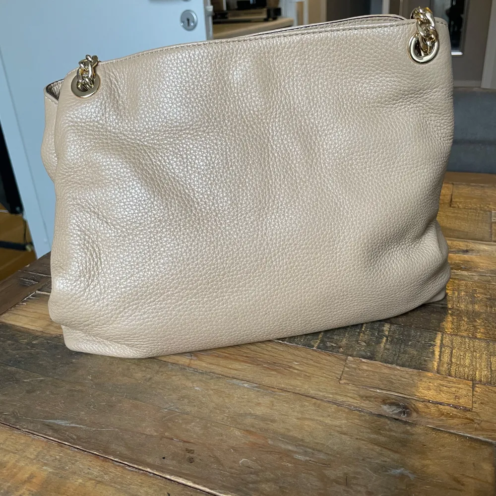 Säljer en snygg beige axelväska från Michael Kors i mycket bra skick. Väskan har en kedjedetalj och en praktisk dragkedja. Perfekt för både vardag och fest! 👜✨B 32cm H 28 cm.. Tröjor & Koftor.