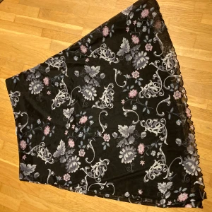 Svart blommig kjol - Säljer en svart kjol med vackert blommönster i rosa och lila toner från Comfort Fashion/cellbes. Kjolen har en svart underkjol och mönstrad mesh utanpå och är perfekt för både vardag och fest. Resår i midjan. Den är i bra skick och passar utmärkt till vår och sommar. 🌸