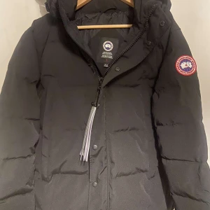 Svart dunjacka från Canada Goose - Säljer en svart dunjacka från Canada Goose 1nt3 autentisk. mycket bra skick. Jackan har en klassisk design med en broderad logga på ärmen och dragkedja framtill. Perfekt för kalla vinterdagar med sin varma och isolerande fyllning. Huvan är justerbar och jackan har flera praktiska fickor. Lappen är ej kvar