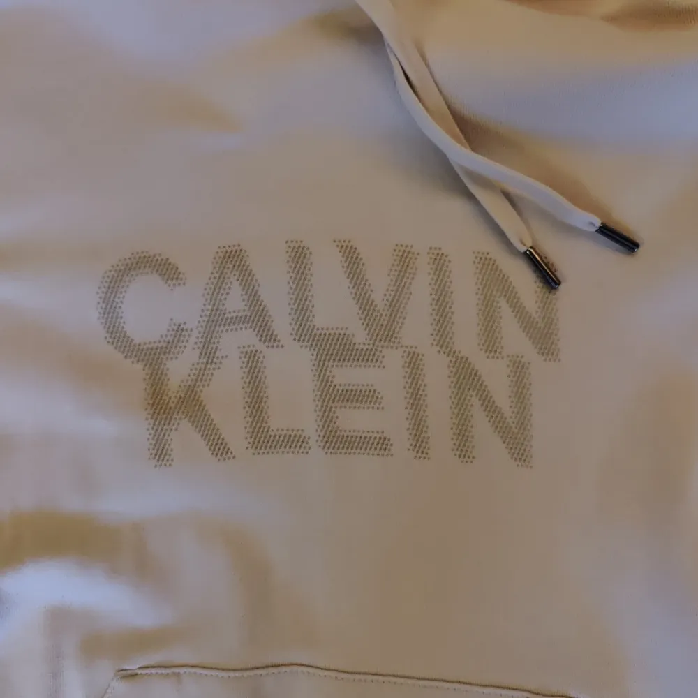 Säljer en snygg beige hoodie från Calvin Klein i storlek S. Den har en klassisk design med en stor ficka fram och justerbar huva. Perfekt för en avslappnad stil och passar till alla årstider. Märket är diskret tryckt på framsidan. Skön och stilren!. Tröjor & Koftor.