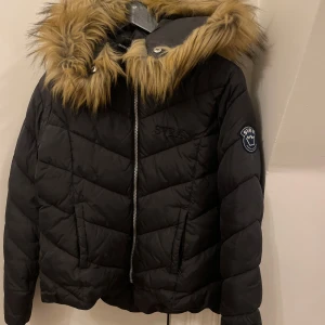 Svart pufferjacka från Svea - Säljer en svart pufferjacka från Svea i mycket bra skick. Jackan har en mysig fuskpäls på huvan och dragkedja framtill. Perfekt för kalla vinterdagar! 🖤Priset kan diskuteras 