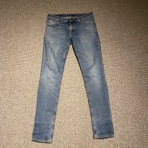 Nudie Jeans - Säljer ett par feta blå jeans från Nudie Jeans i bra skick då jag inte använder de så ofta längre. De har en skön passform med slitna detaljer. 29:32