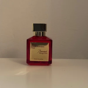 Baccarat Rouge 540 Extrait de Parfum - Säljer en lyxig parfymflaska av Baccarat Rouge 540 Extrait de Parfum från Maison Francis Kurkdjian. Flaskan är fyrkantig och röd med en elegant guldetikett och svart kork. Perfekt för den som vill ha en exklusiv doftupplevelse.