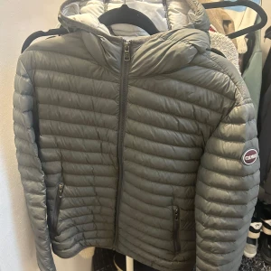 Grå dunjacka från Colmar - Säljer en snygg grå dunjacka från Colmar i mycket bra skick. Jackan har en quiltad design med dragkedja framtill och en mysig huva, den har ett litet hål i högra jack fickan, inget man ser utifrån, därmed är priset billigare 