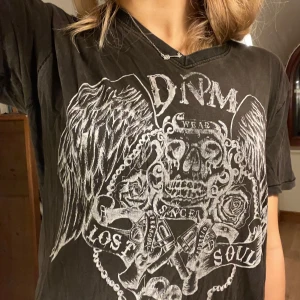 Svart t-shirt med tryck - Cool svart t-shirt från DNM med ett stort tryck av en dödskalle, vingar och rosor i vitt. Den har en normal passform och korta ärmar. 