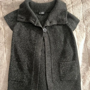 Grå stickad väst med knappar ONLY - Säljer en grå stickad väst- tröja med knappar framtill (3st). Den har en hög krage och 2 små fickor. Perfekt för lager-på-lager under hösten eller vintern. Man kan själv välja hur den ska sitta vilket jag älskar (bild exempel). Används ej längre och därför säljer jag, typ i nyskick inga skador osv.