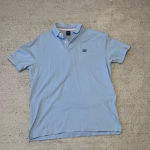 Boggi Milano piké - Säljer en stilren ljusblå pikétröja från Boggi Milano i bra skick. Tröjan har korta ärmar och en klassisk krage med knappar. Den är tillverkad i bomull och har en broderad logga på bröstet. Perfekt för vår och sommar!