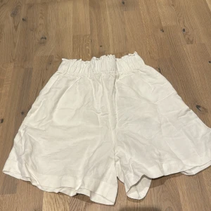 Vita linne shorts från H&M - Säljer ett par vita shorts från H&M i nytt skick. De är högmidjade med en elastisk midja för extra komfort. Perfekta för sommardagar eller en avslappnad vårlook. Materialet är lätt och luftigt, vilket gör dem idealiska för varmare väder.