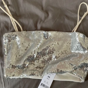 Glittrig tubtopp i silver - Säljer en superglittrig tubtopp i silver med paljetter över hela ytan. Perfekt för fest eller nyår! Den har tunna axelband och har en tight passform. Toppen är i nytt skick och har fortfarande etiketten kvar. Gör dig redo att glänsa! ✨🤍