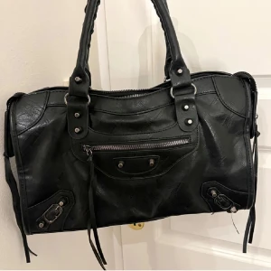 Svart axelväska med dragkedja - Snygg svart axelväska med coola detaljer och dragkedja framtill. Perfekt för både vardag och fest! Den har två rejäla handtag och en stilren design som passar till allt. Väskan är i mycket bra skick och redo för nya äventyr.(lånad bild) 