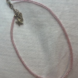 Rosa pärlhalsband med sjöstjärneberlock - Sött rosa pärlhalsband med små pärlor och en charmig sjöstjärneberlock i silver. Perfekt för sommarens alla äventyr eller som en fin detalj till vardagsoutfiten. Halsbandet har en justerbar kedja för perfekt passform.