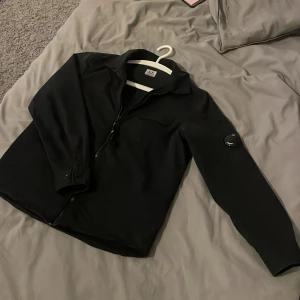 Svart jacka från C.P. Company - Säljer en stilren svart jacka från C.P. Company. Den har en dragkedja framtill. Perfekt för höst och vår, den passar till både vardag och en sen sommar kväll. Jackan är i mycket bra skick och har en normal passform. Perfekt för dig som vill ha en snygg och funktionell jacka! Size 10 år. Pris kan diskuteras.