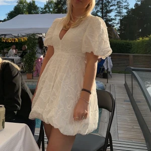 Studentklänning!! - Säljer en superfin vit klänning med puffiga kortärmar och v-ringning. Den har ett vackert blommigt mönster och är perfekt för sommarens alla studentfester. Klänningen är i ett bra skick och har en normal passform. Klänningen har några sminkfläckar vid urringningen som går att tvätta bort!