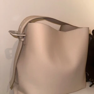 Beige axelväska från Mango - Säljer en stilren beige axelväska . Väskan har en enkel design med ett justerbart axelband och en slät yta. Perfekt för vardagsbruk och passar till de flesta outfits. Den är i mycket bra skick och redo för en ny ägare!