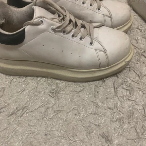 Vita sneakers med svart detalj - Säljer ett par vita sneakers i bra skick med svart detalj på hälen. De har snörning och är perfekta för vardagsbruk. Skorna är bekväma och stilrena, passar till det mesta i garderoben. Lite smuts på sulan men inget som inte går att fixa. Perfekta för både vår och höst!