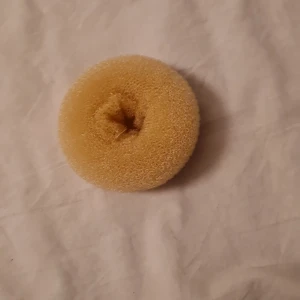 Beige hårdonut - Säljer en beige hårdonut perfekt för att skapa snygga och fylliga hårknutar. Den är gjord av ett lätt och luftigt material som ger bra volym utan att kännas tungt. Perfekt för både vardag och festliga tillfällen! Aldrig använt. Typ gul beige 