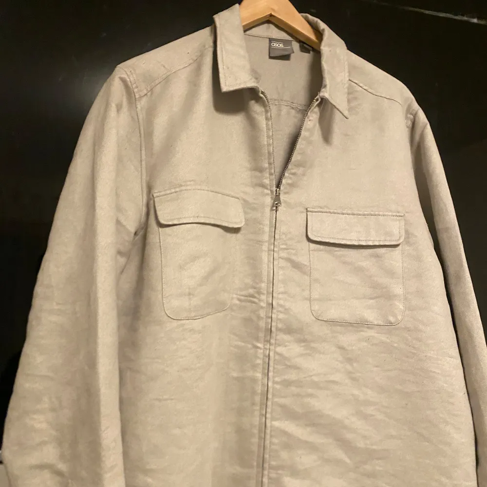 Säljer en snygg beige overshirt från asos. Den har en dragkedja framtill och två praktiska bröstfickor med lock. Perfekt för lager-på-lager-stil under hösten eller våren. Materialet känns slitstarkt och bekvämt. Passar både till vardags och lite mer uppklädda tillfällen. 🧥✨. Jackor.