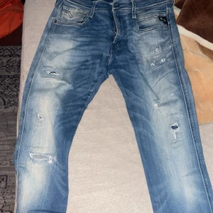 Blå jeans från Replay - Säljer ett par snygga blå jeans från Replay i storlek M. De har en cool slitning och en klassisk femficksdesign. Perfekta för en avslappnad stil och passar till både vardag och fest. Midjan är 30 och längden 34. Sköna och stilrena!