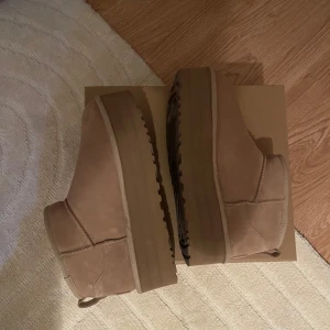 Beige UGG platform - Säljer ett par supermysiga beige UGG boots i storlek 39. De är i nytt skick och har en mjuk pälsfodring som håller fötterna varma under kalla dagar. Perfekta för höst och vinter! De har en klassisk design med en robust sula för extra komfort.