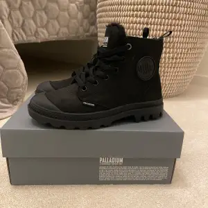 Säljer ett par svarta Palladium boots i mycket bra skick. De har en robust sula och är fodrade med päls för extra värme. Skorna har både snörning och dragkedja för enkel på- och avtagning. Perfekta för höst och vinter! 