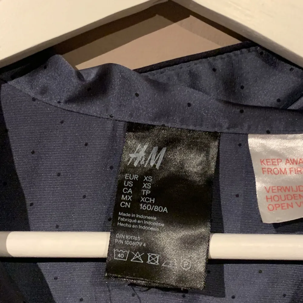 Säljer en elegant blå pyjamas från H&M i storlek XS. Den har ett diskret prickigt mönster och är tillverkad i ett glansigt material som ger en lyxig känsla. Blusen har långa ärmar och en klassisk krage, perfekt för både vardag och fest. Knappar framtill för en stilren look.. Övrigt.